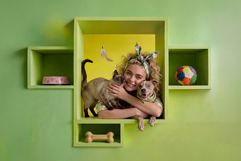 Uśmiechnięta kobieta z psem i kotem na zielonym tle. Grafika promująca wydarzenie „Targi dla Zwierząt\