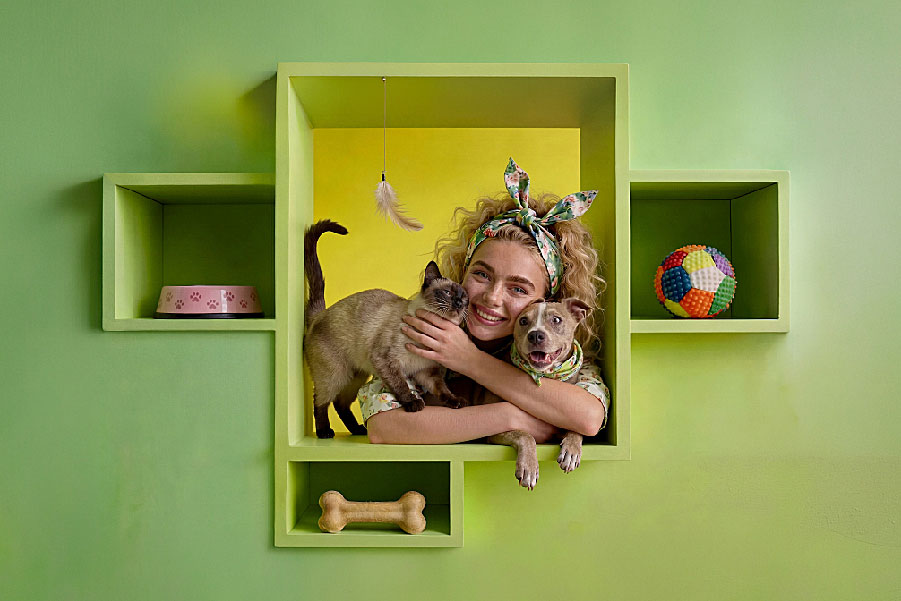 Uśmiechnięta kobieta z psem i kotem na zielonym tle. Grafika promująca wydarzenie „Targi dla Zwierząt\