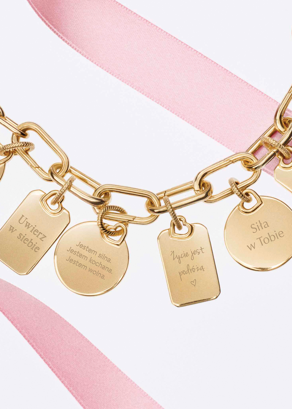 Otwarcie salonu Pandora w Galerii Solnej – złota bransoletka z grawerowanymi zawieszkami z inspirującymi hasłami na różowym tle, promująca personalizowaną biżuterię.
