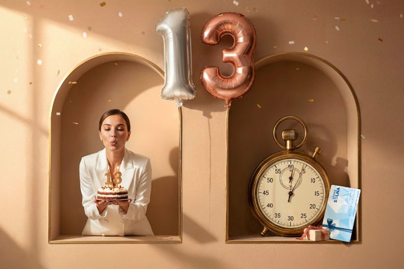 Kobieta z tortem urodzinowym i balony z liczbą 13 promujące akcję Szczęśliwa 13-tka w Galerii Solnej.