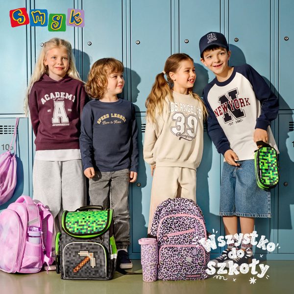 Szkolny baner promocyjny sieci Smyk z hasłem „Wszystko do szkoły”. Czwórka dzieci stoi na tle niebieskich szafek szkolnych: blond dziewczynka w fioletowej bluzie z kapturem, chłopiec w granatowej bluzce z długim rękawem, dziewczynka w beżowej bluzie oraz chłopiec w beżowo-granatowej bluzce i czapce z daszkiem. Przed dziećmi stoją plecaki i piórniki: różowy plecak z bidonem, szary plecak i piórnik w pikselowy wzór z motywem z gry Minecraft (kilof), plecak w fioletową panterkę z bidonem oraz drugi piórnik z motywem Minecraft. W lewym górnym rogu umieszczono kolorowe logo „SMYK”.